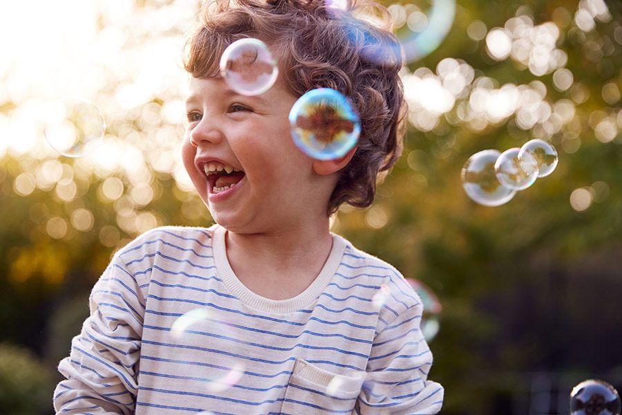 Individual Life Insurance - Young Boy Having Fun In Garden Chasing And Bursting Bubbles